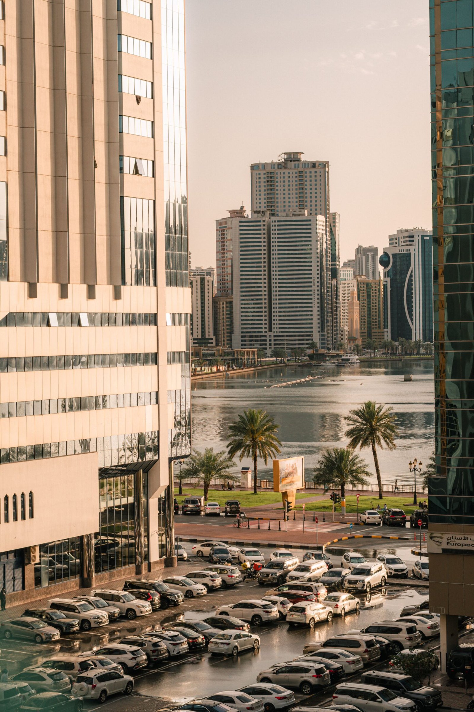 Aerial view of Dubai skyline with parking lot and waterfront, framed by skyscrapers during the day.