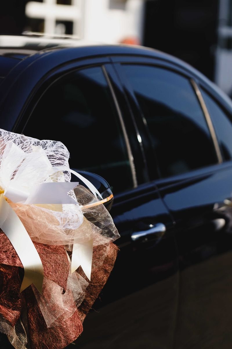 Close-up of a black wedding car decorated with elegant ribbons and bows.