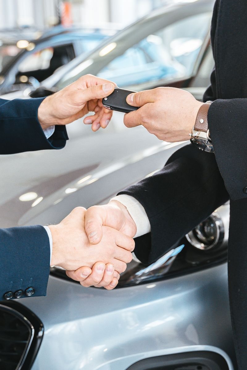 Two businessmen shaking hands and exchanging car keys in a dealership. Symbolizes a successful deal.