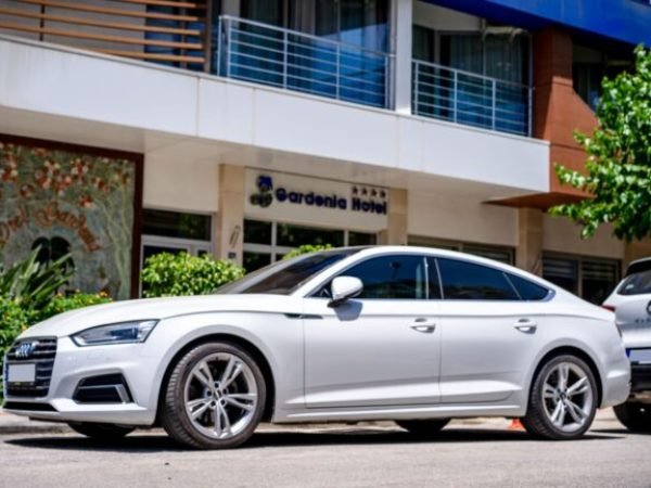 White luxury car parked in front of a hotel with modern architecture.